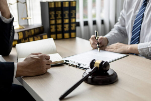 A defamation solicitor meeting with a client to sign legal documents with a gavel and law books on the table.