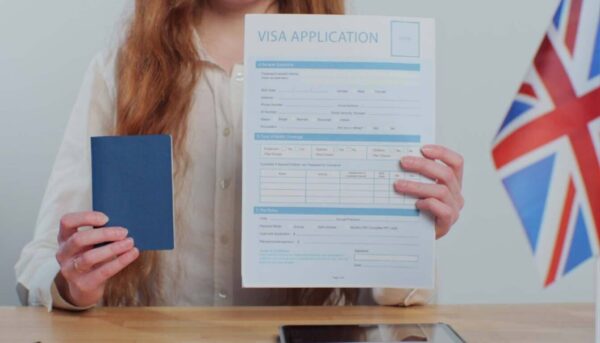 Person holding a passport and a UK visa application form with a UK flag visible, relating to British citizenship or visa application.