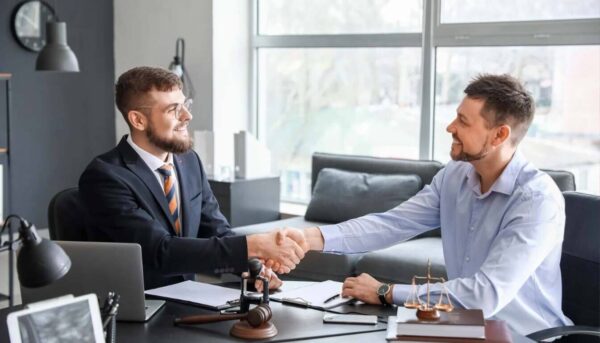 Two professionals, possibly a lawyer and client, shaking hands across a desk, signifying legal advice or final agreement on ILR application.