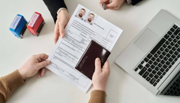 Hands reviewing a visa application form and passport with Approved and Rejected stamps nearby.