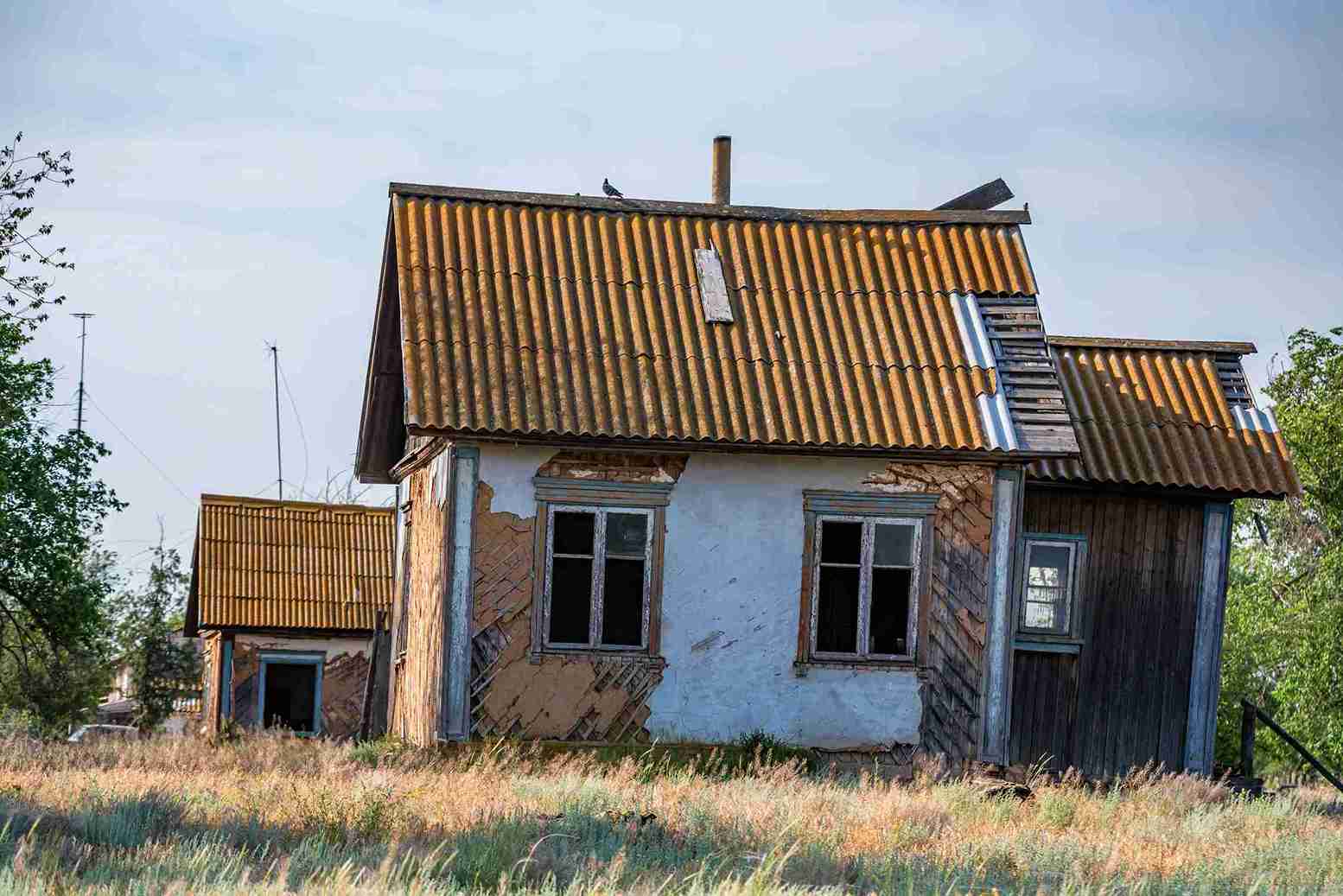 An old house with a tin roof stands alone in a field, highlighting the theme of housing disrepair