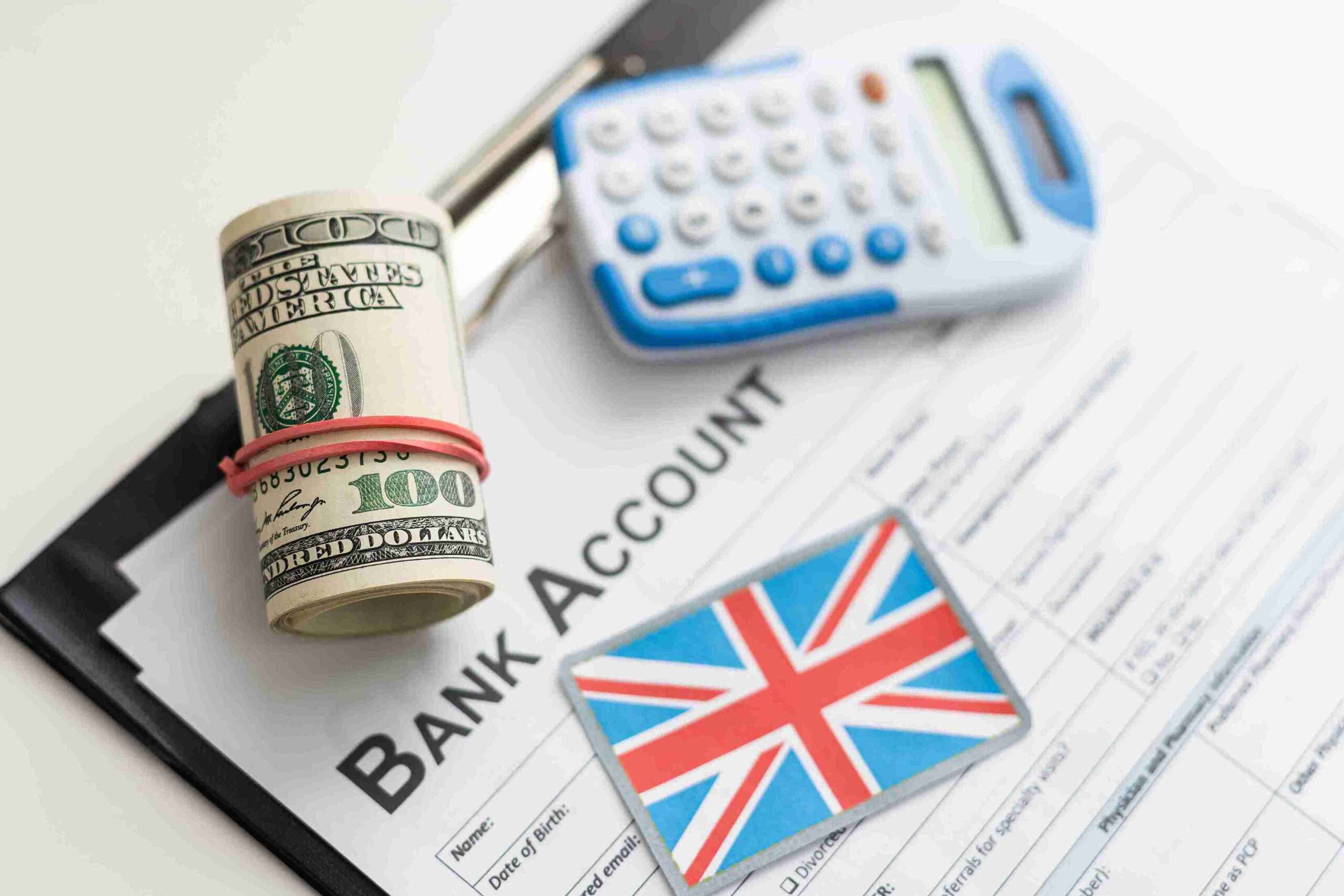 A wad of bills on a bank account application, with a calculator and a small Union Jack flag. The scene conveys financial stability for sponsor license