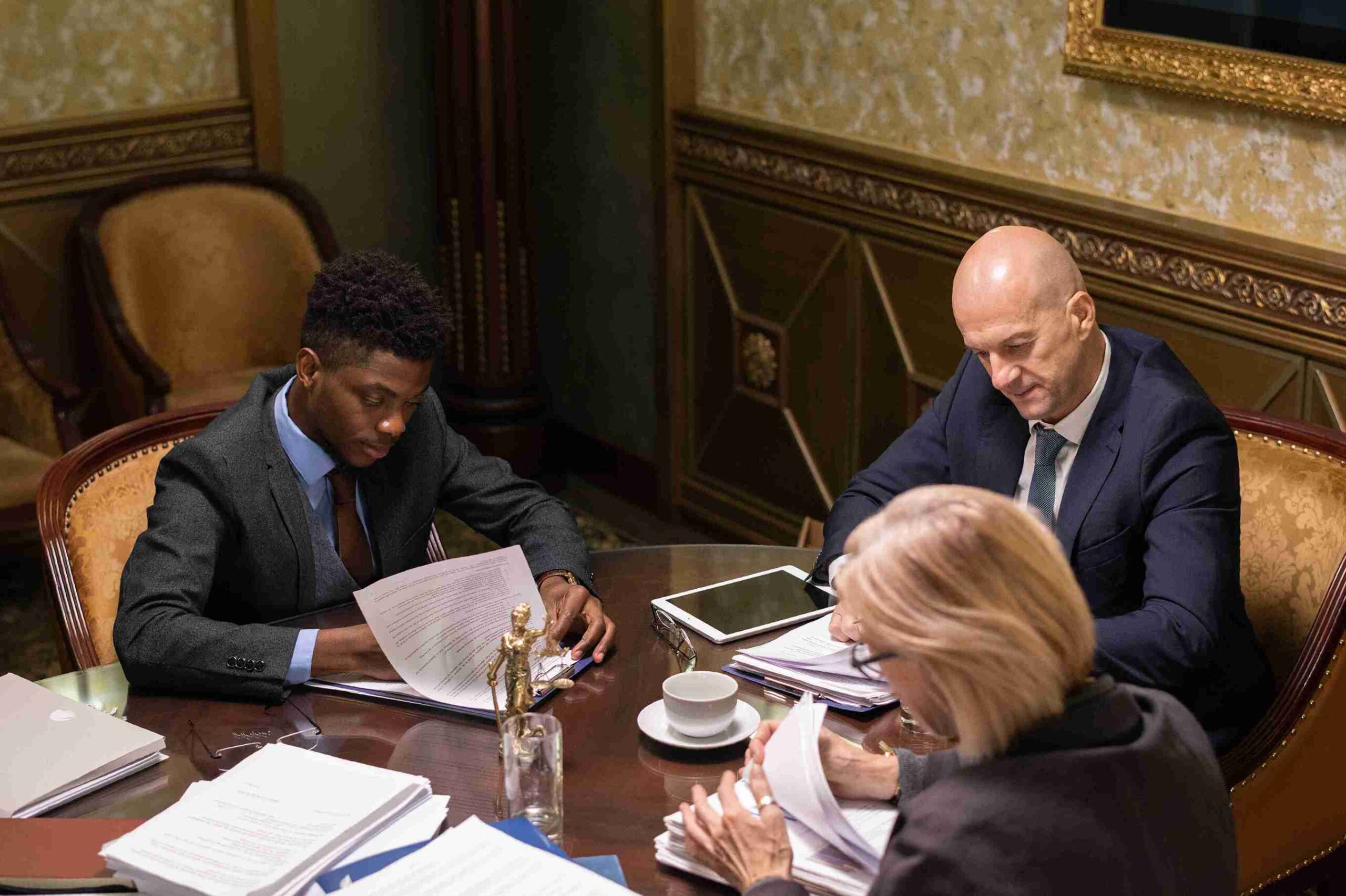 Three lawyer collaborate at a table, reviewing documents and working on laptops.