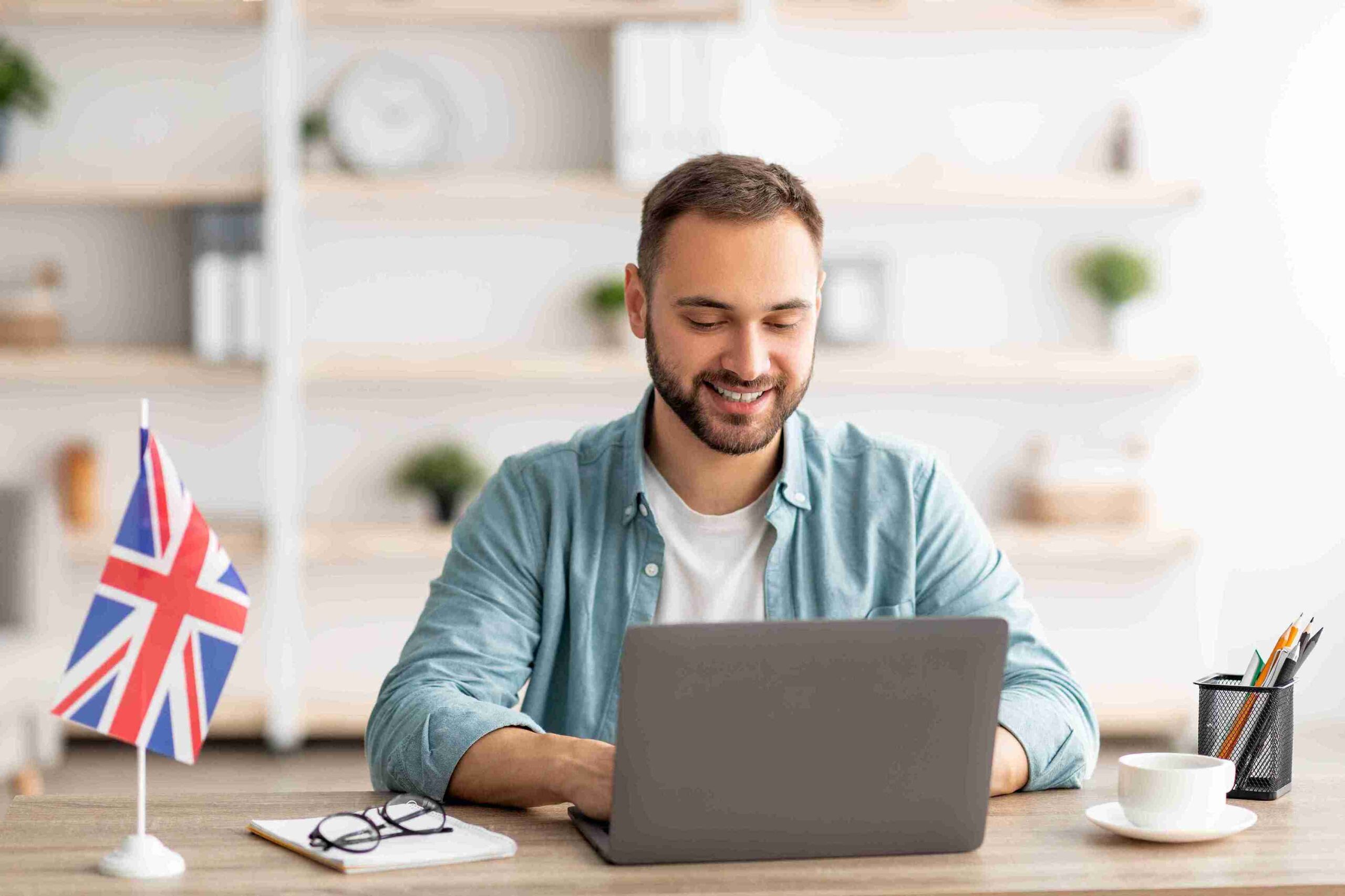 A man typing on his laptop, set against the backdrop of the British flag, symbolizing a connection to the UK.