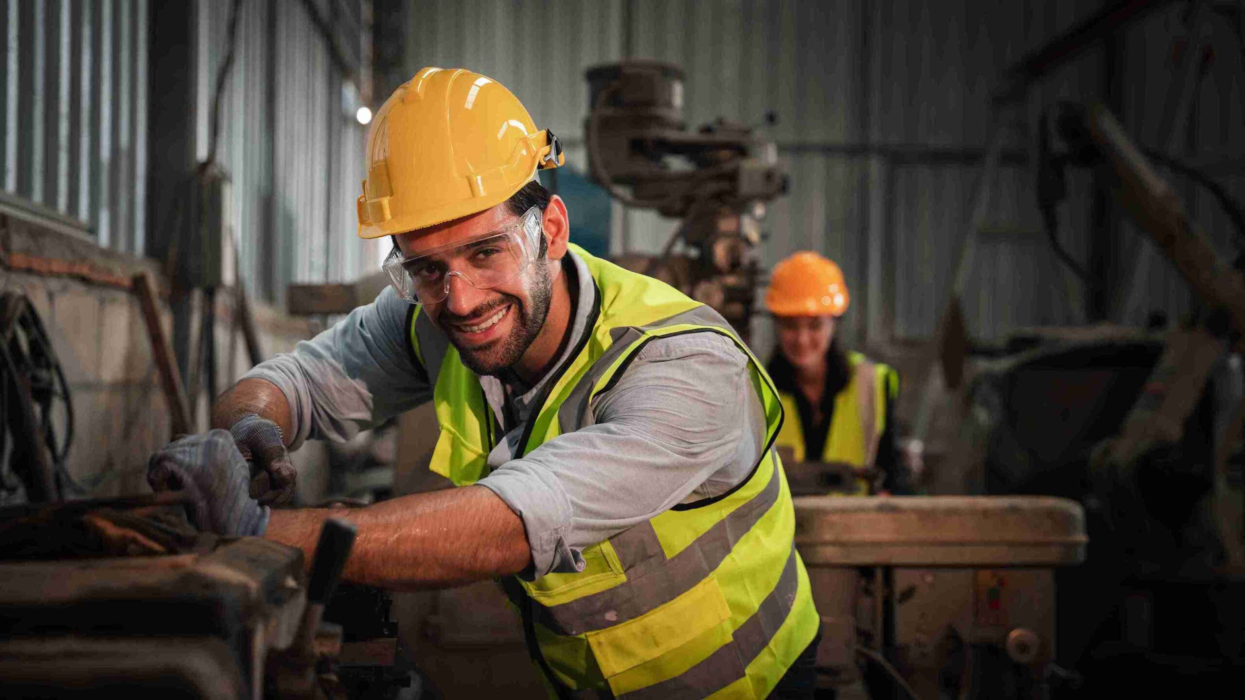 A man in a hard hat and yellow vest operates a machine, focused on his work in a construction environment.