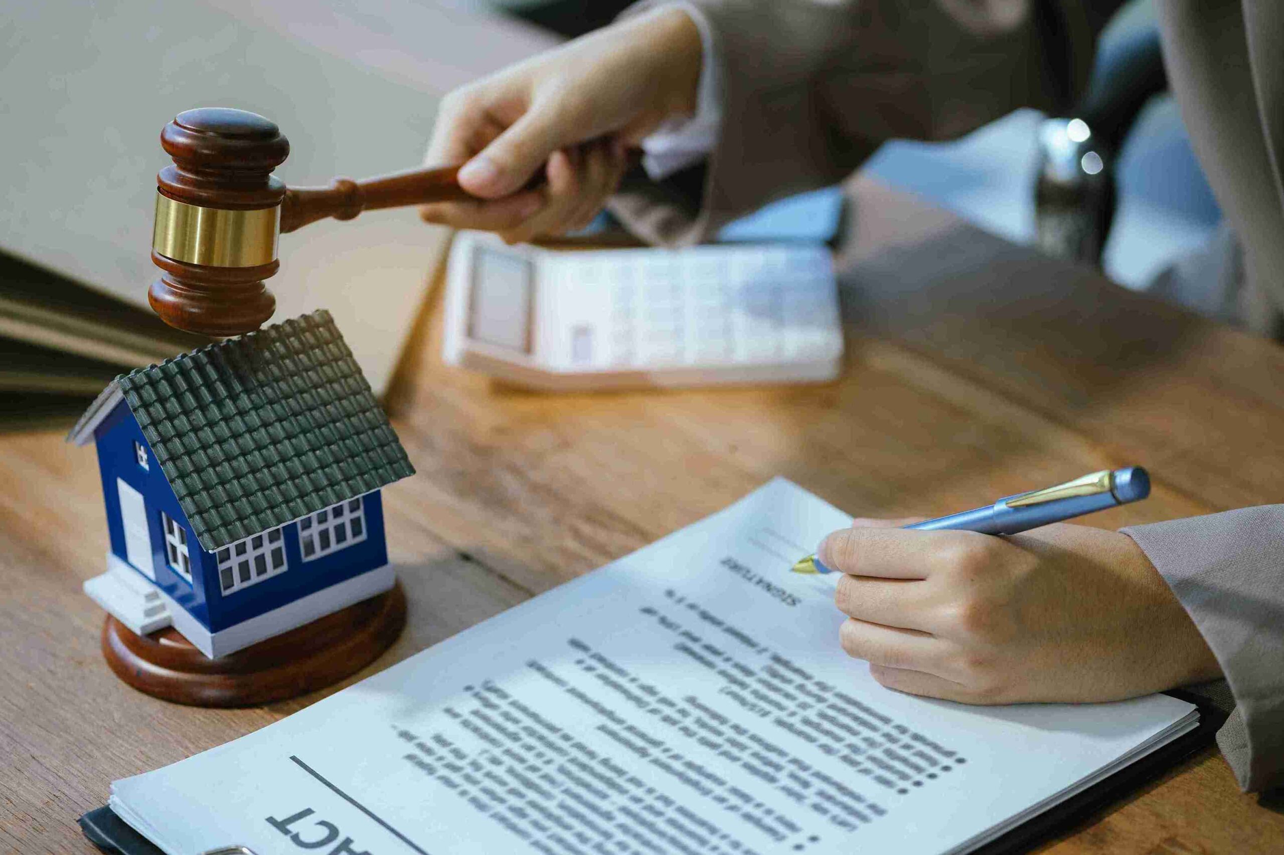 A person signing a contract next to a house model, highlighting Housing Disrepair Claims for safe, secure homes in the UK.