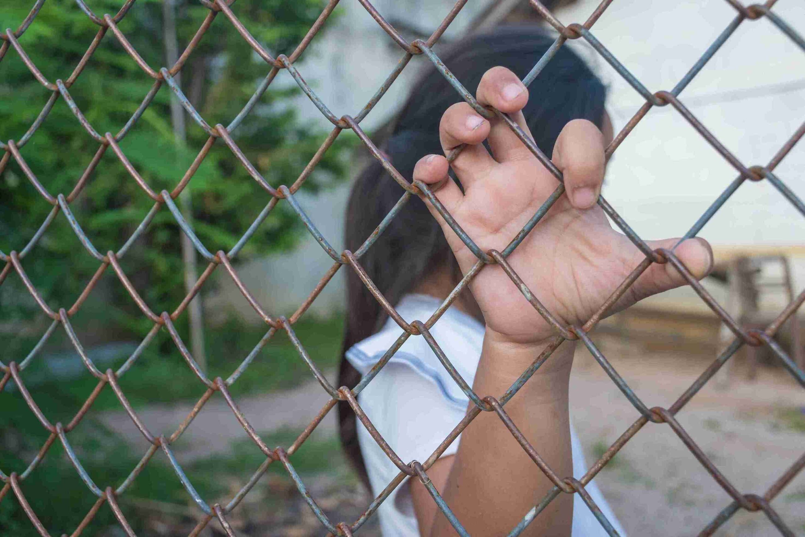 A person reaches through a chain link fence, symbolizing barriers faced in human trafficking.