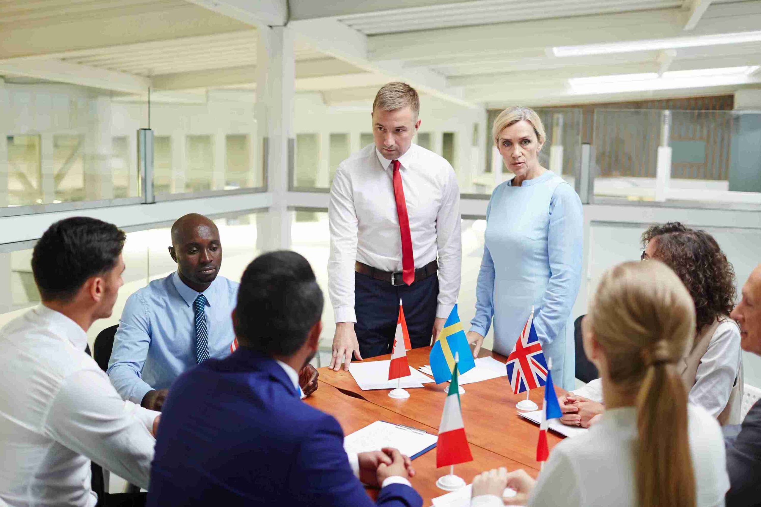A diverse group of people gathered around a table, discussing UK ancestry visa options, with flags displayed in the background.