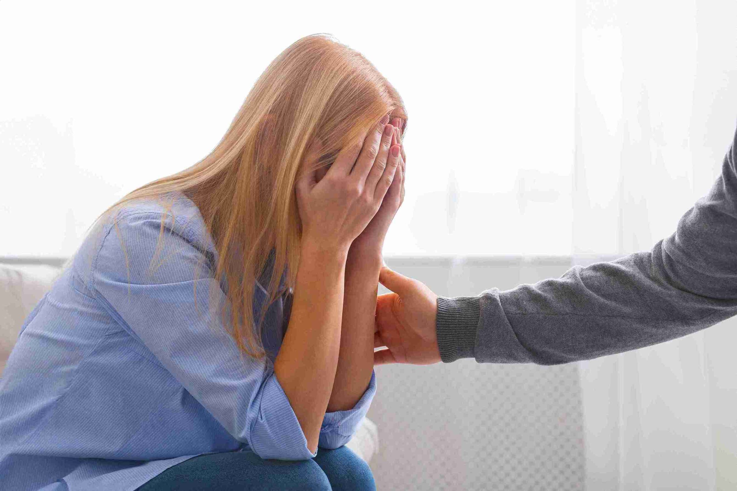 A woman in distress, crying and covering her face, is guided by a therapist addressing domestic violence issues.