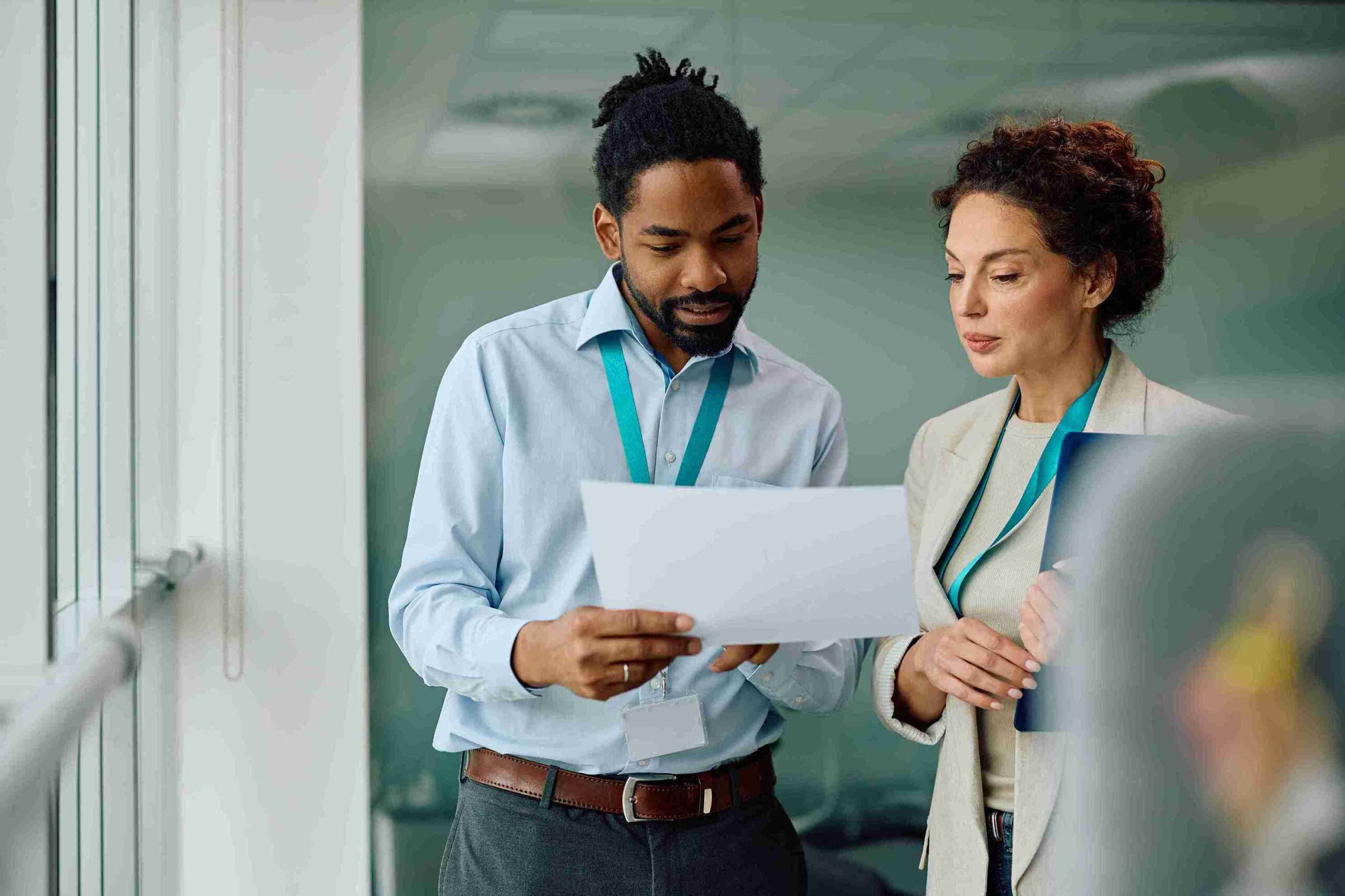A man and woman in professional attire review a document together in an office setting for approval of sponsorship conveying focus and collaboration