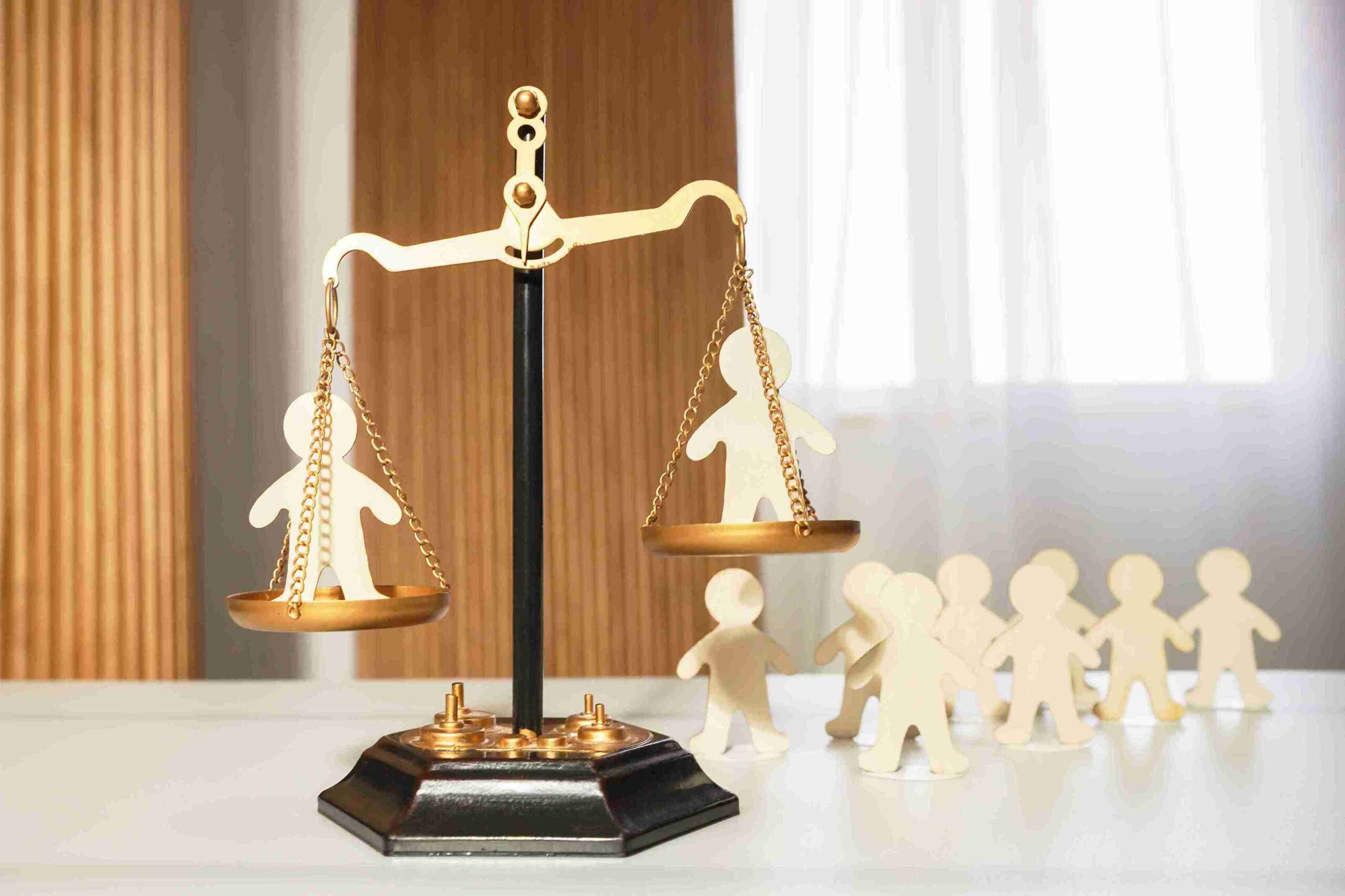A scale balancing paper cutouts of people on a wooden table, symbolizing equality and representation.