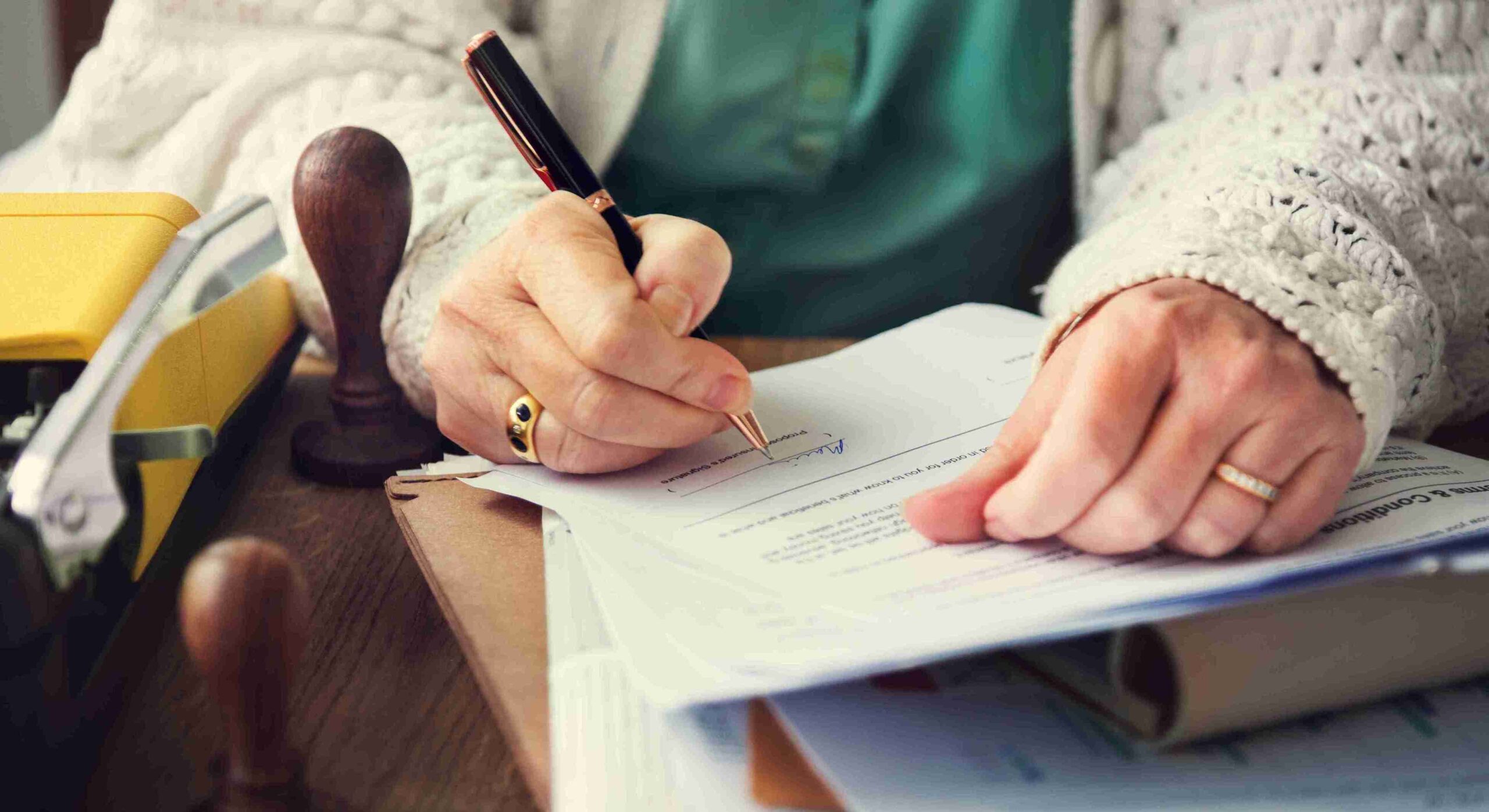 Person signing a document at desk with stamp and stapler, representing a correctly drafted Will meeting legal requirements in Wales.