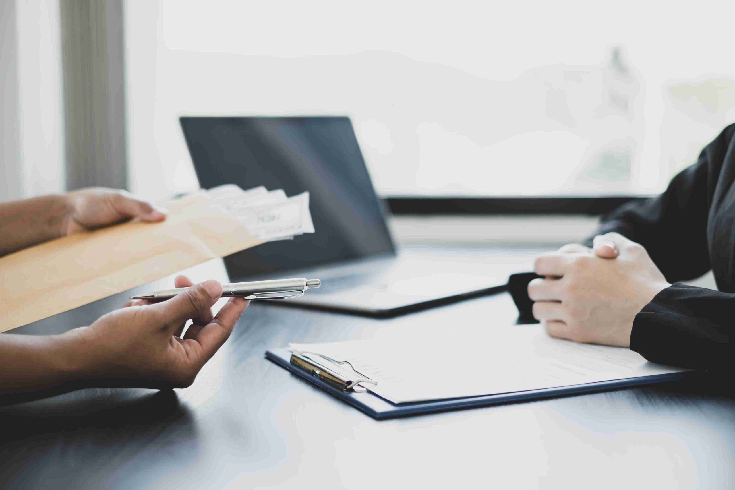 Two people at a desk exchanging documents and pen, representing preparing and submitting an appeal or administrative review.