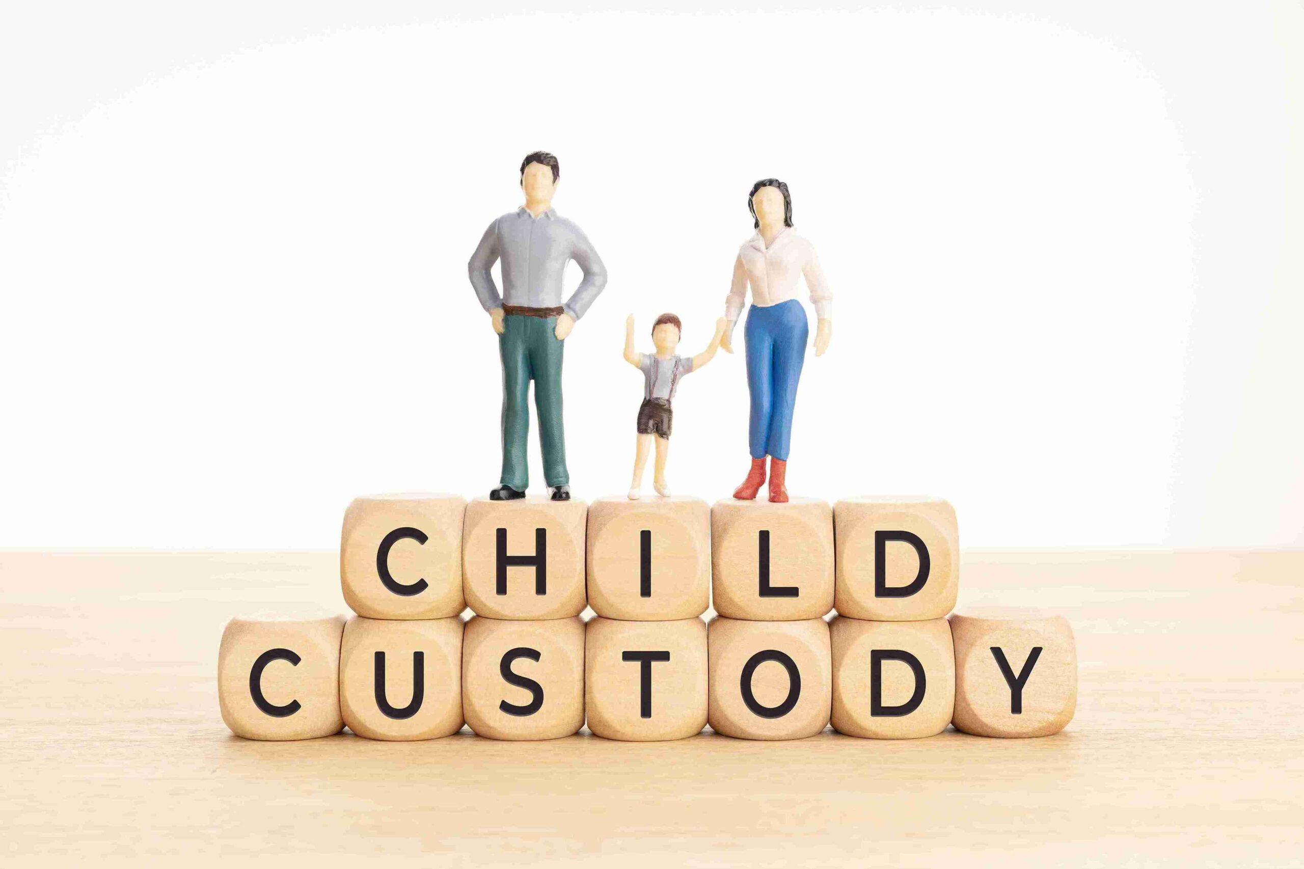 Miniature figures of two adults and a child stand atop wooden blocks spelling "CHILD CUSTODY," conveying themes of family and legal issues.