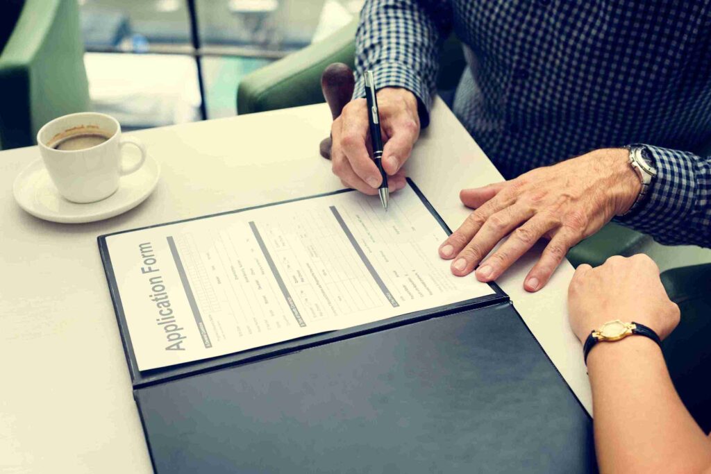 A couple sitting at a table, focused on filling out a mortgage application together, with documents and a laptop in front of them.