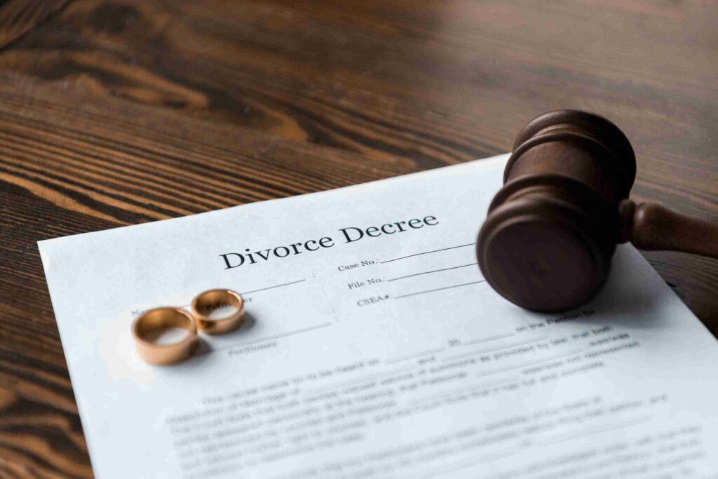 Wooden gavel and wedding rings resting on a divorce decree paper on a wooden table, conveying a sense of legal formality and emotional closure.