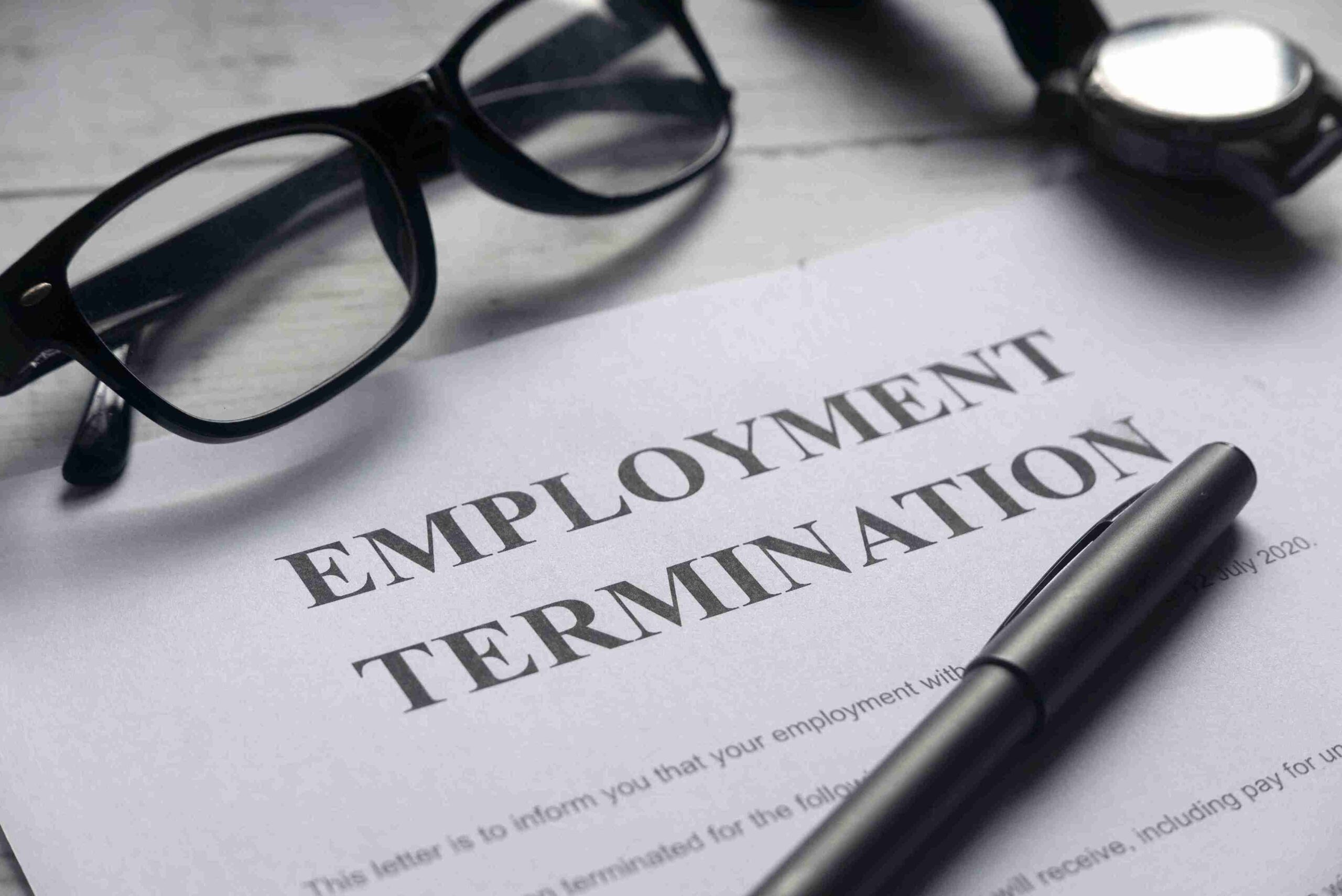 A paper titled Employment Termination lies on a desk with glasses and a pen beside it, suggesting a serious, official tone.