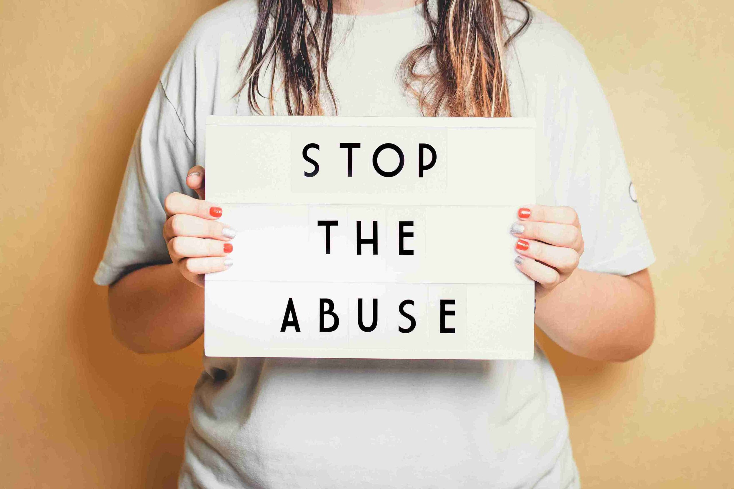 Person holding a sign reading "Stop the Abuse," expressing a strong anti-abuse message. The background is neutral, emphasizing the message.