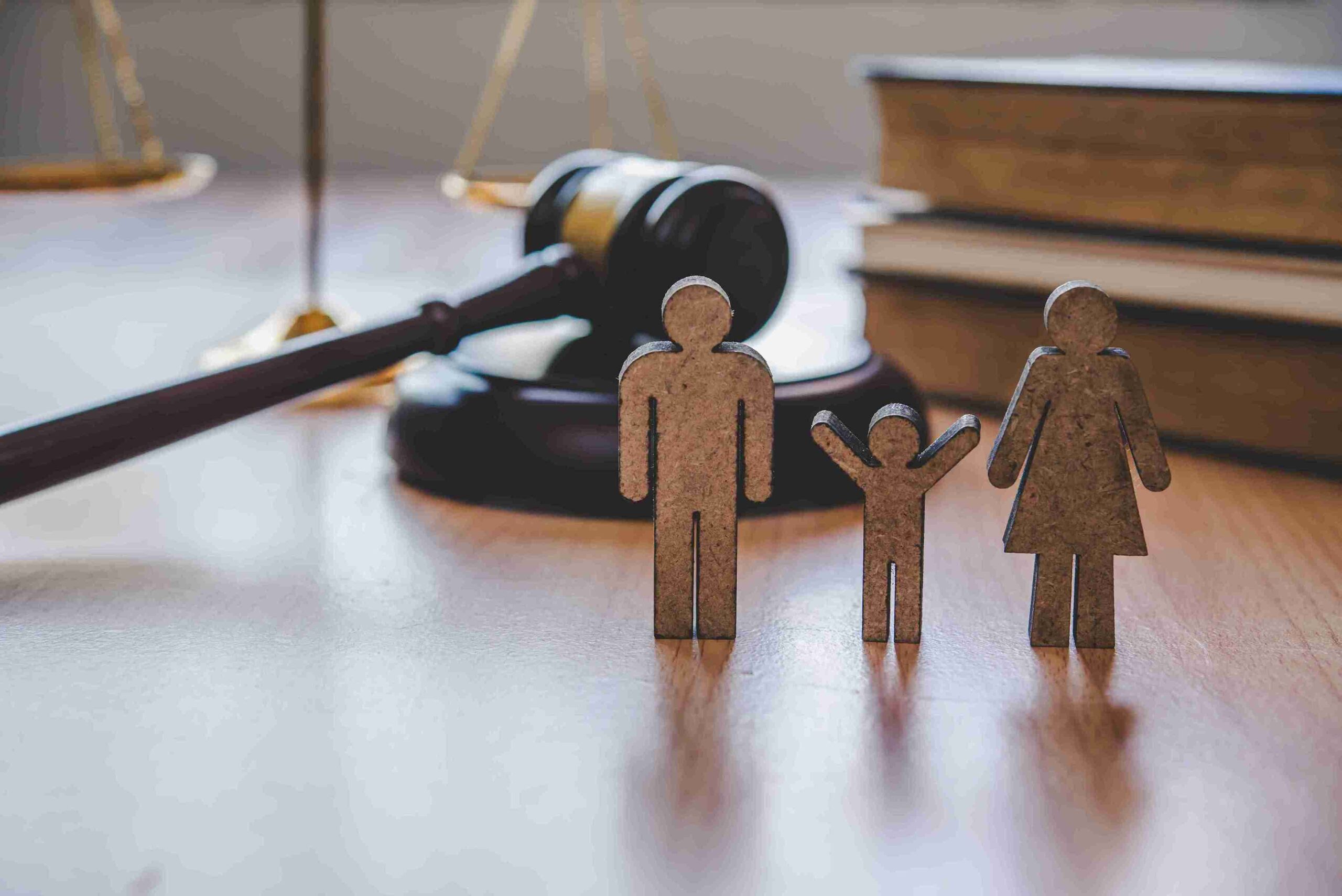 Wooden family figures with a child stand on a table near a judge's gavel and legal books, symbolizing legal and family matters.