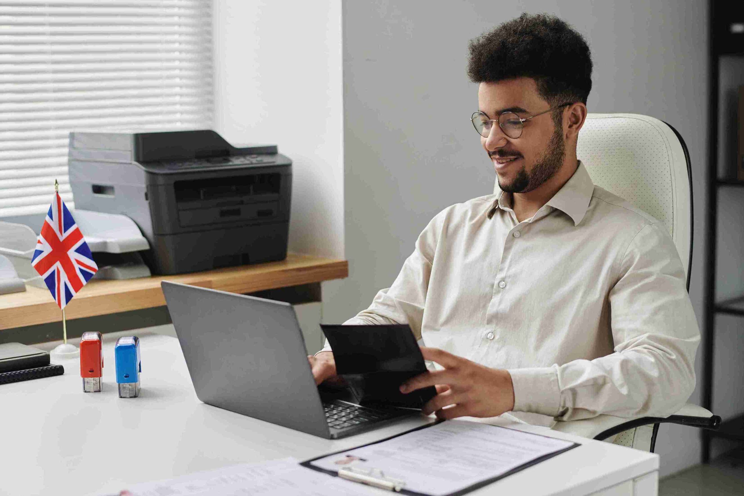 A man in a white shirt sits at a desk with a laptop, preparing his indefinite leave to remain application.
