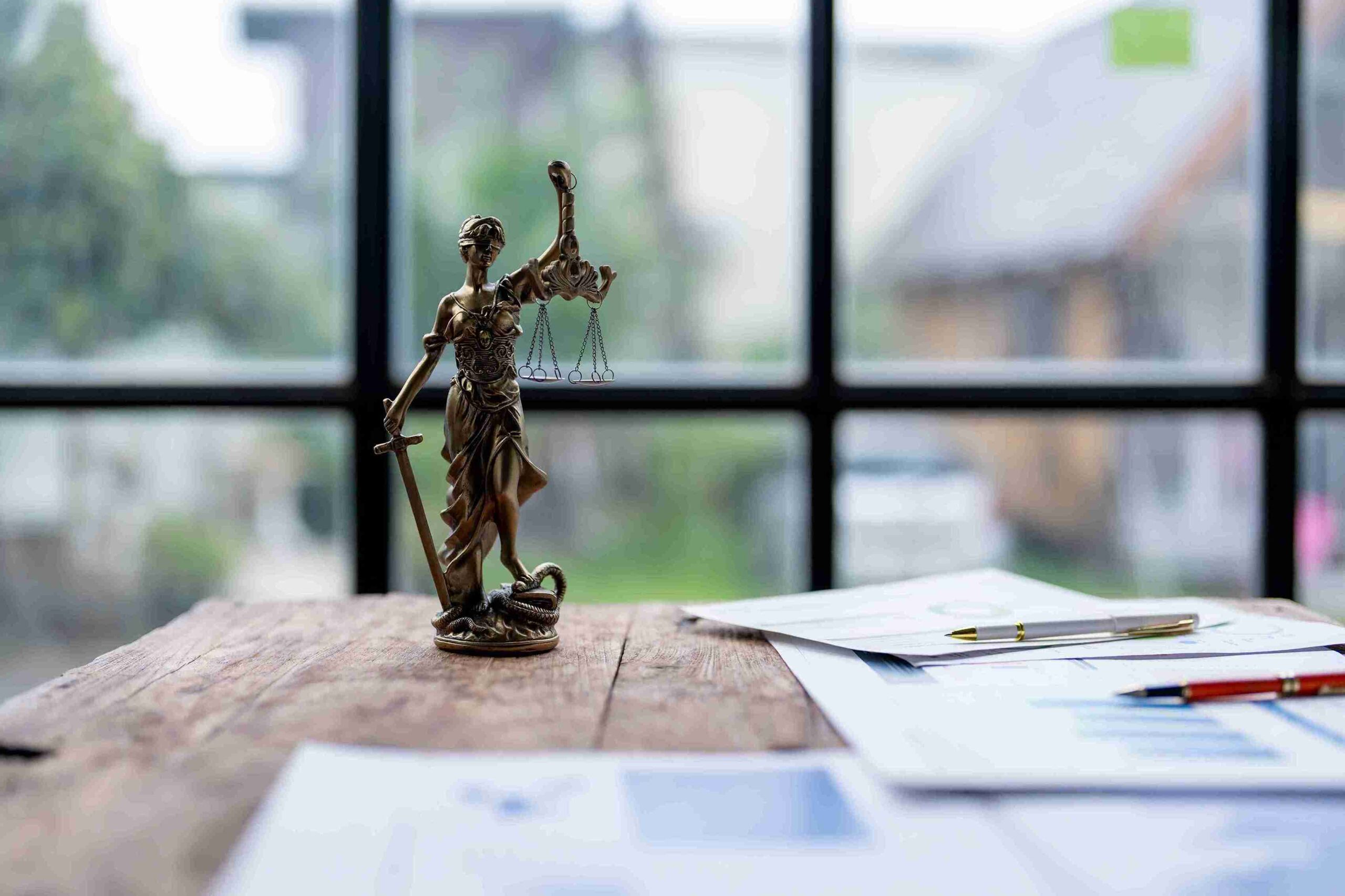 A statue of Lady Justice stands on a desk, illuminated by natural light from a nearby window.