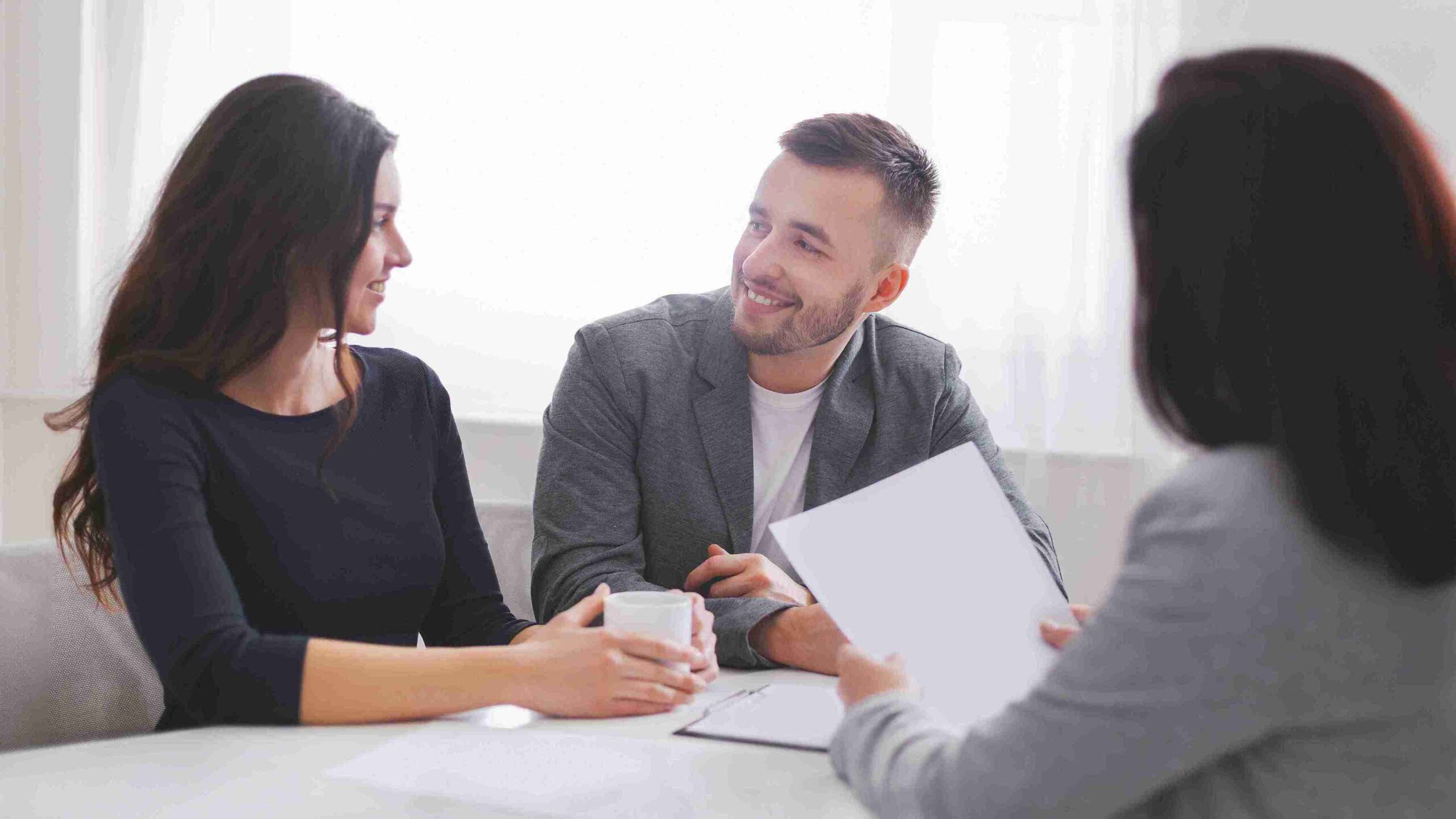A man and woman meet with a suited man, discussing immigration applications and necessary documentation for approval.