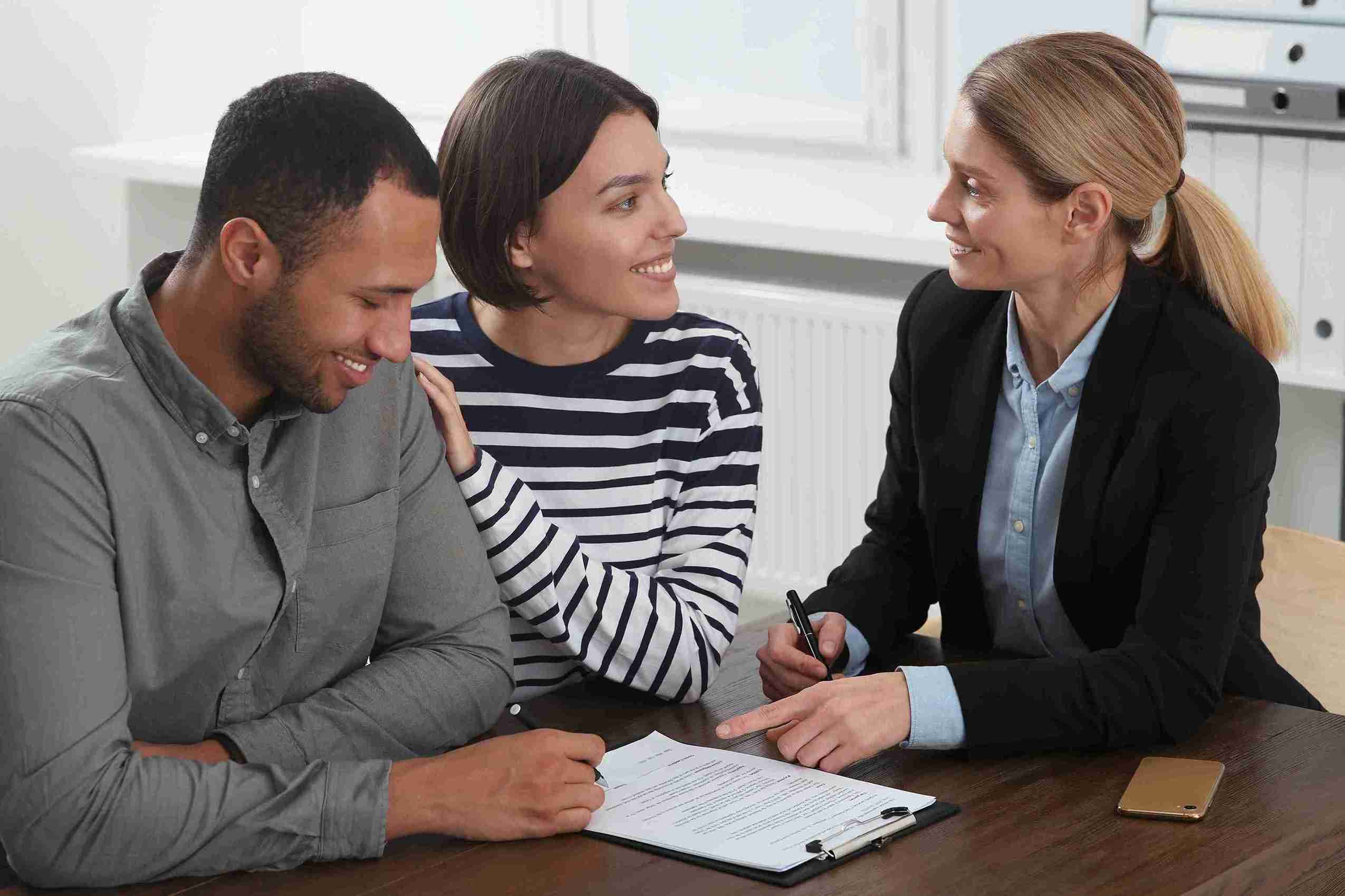 A couple and a man and woman sit at a table, reviewing and signing paperwork for a UK Spouse Visa application.