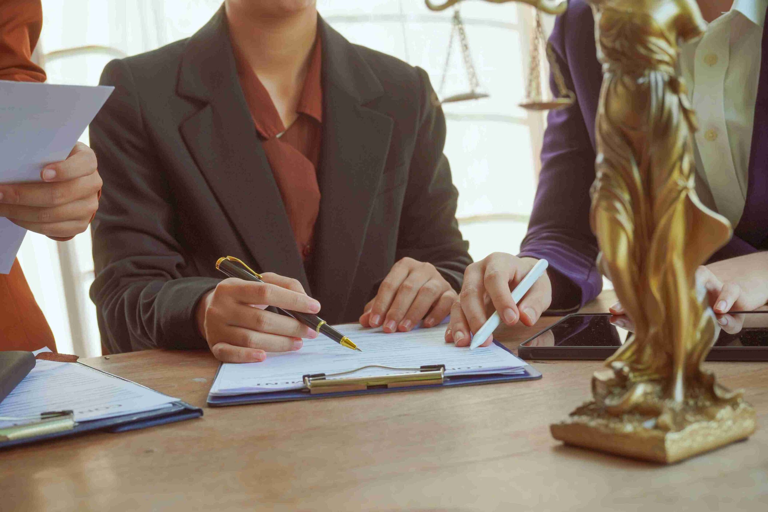 Three business professionals discuss documents at a table, with a statue of a woman prominently displayed among them.