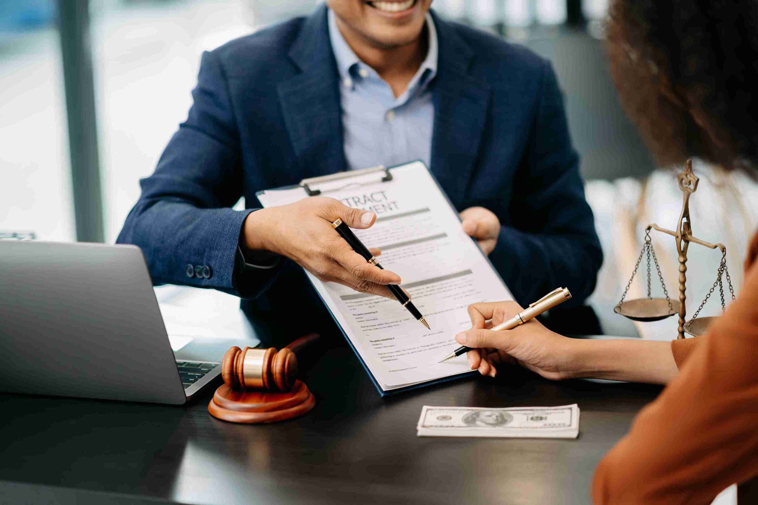 A lawyer and client are seated at a table, signing a contract together, with focused expressions on their faces.