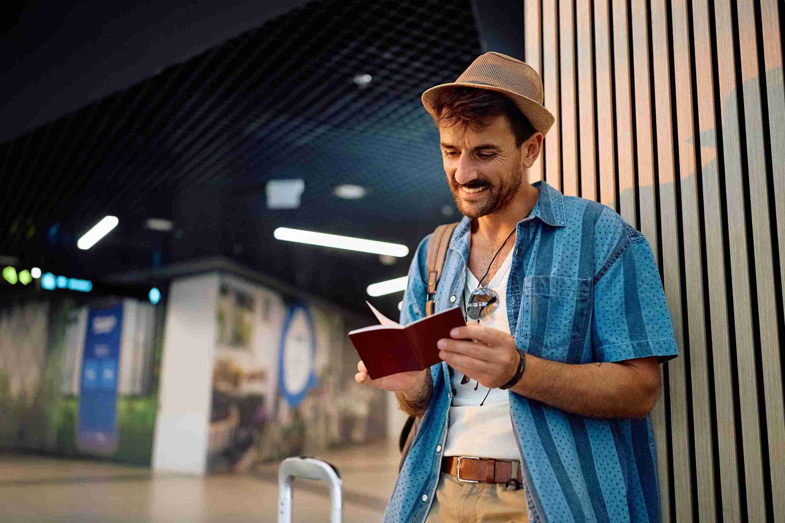 A man wearing a hat checks his phone while holding a suitcase, appearing focused and ready for travel.