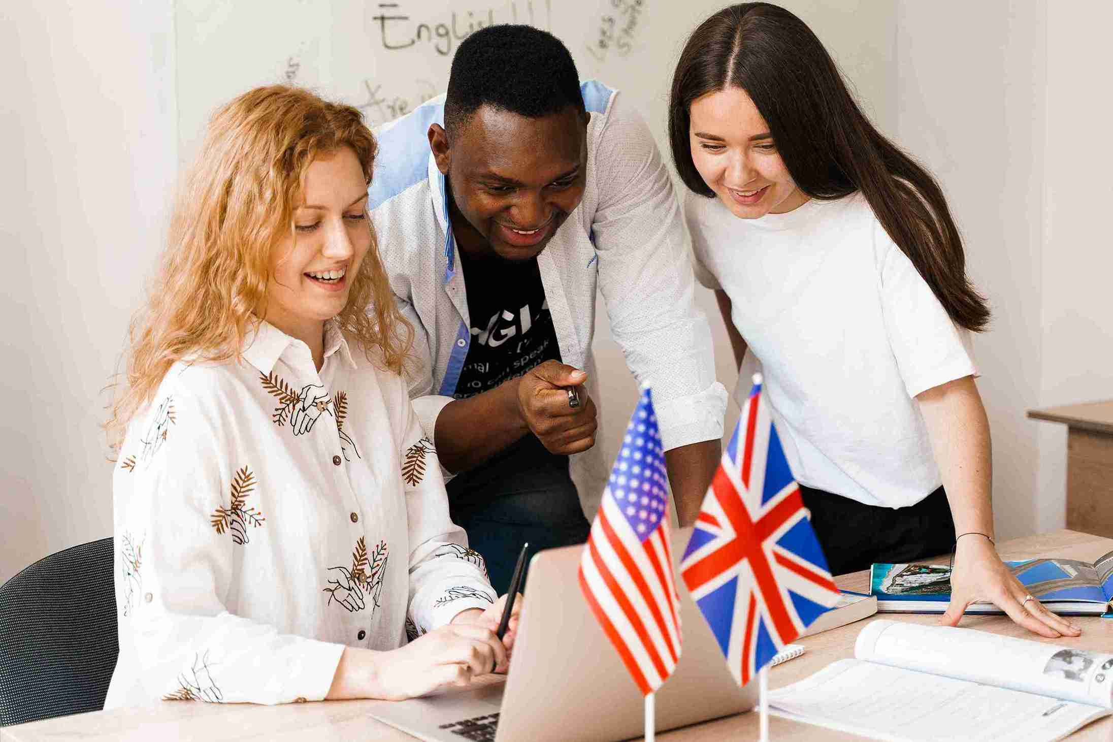 Three people gather around a laptop displaying various flags, engaged in discussion and collaboration.