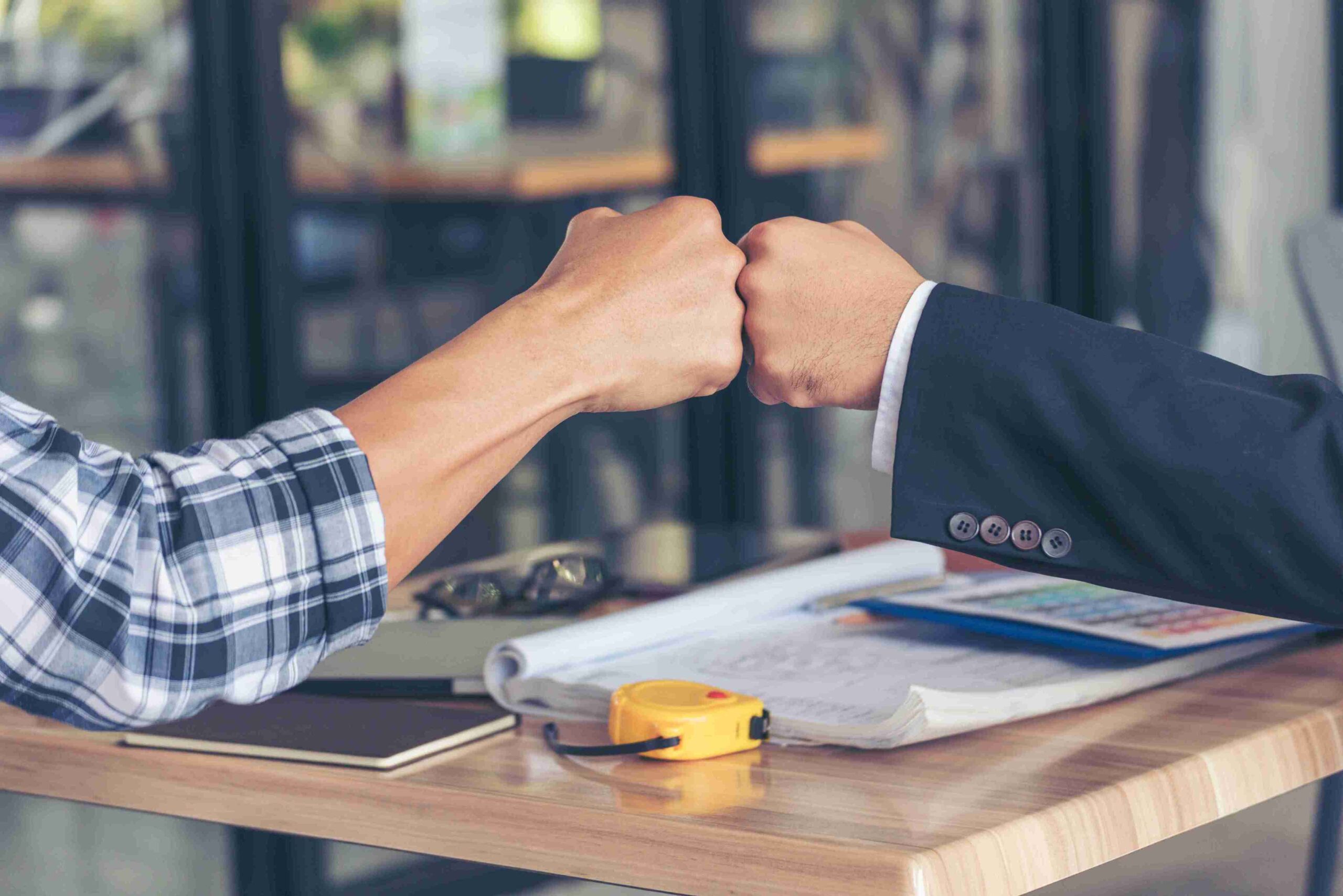 Two people shaking hands across a table, symbolizing agreement or partnership in a professional setting.