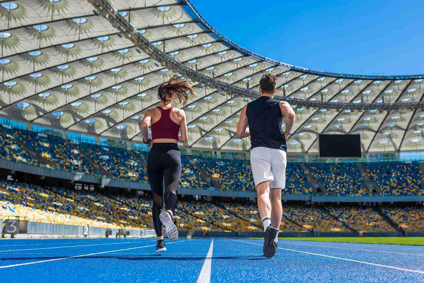 Two runners sprinting on a track inside a vibrant arena, showcasing athleticism and determination.