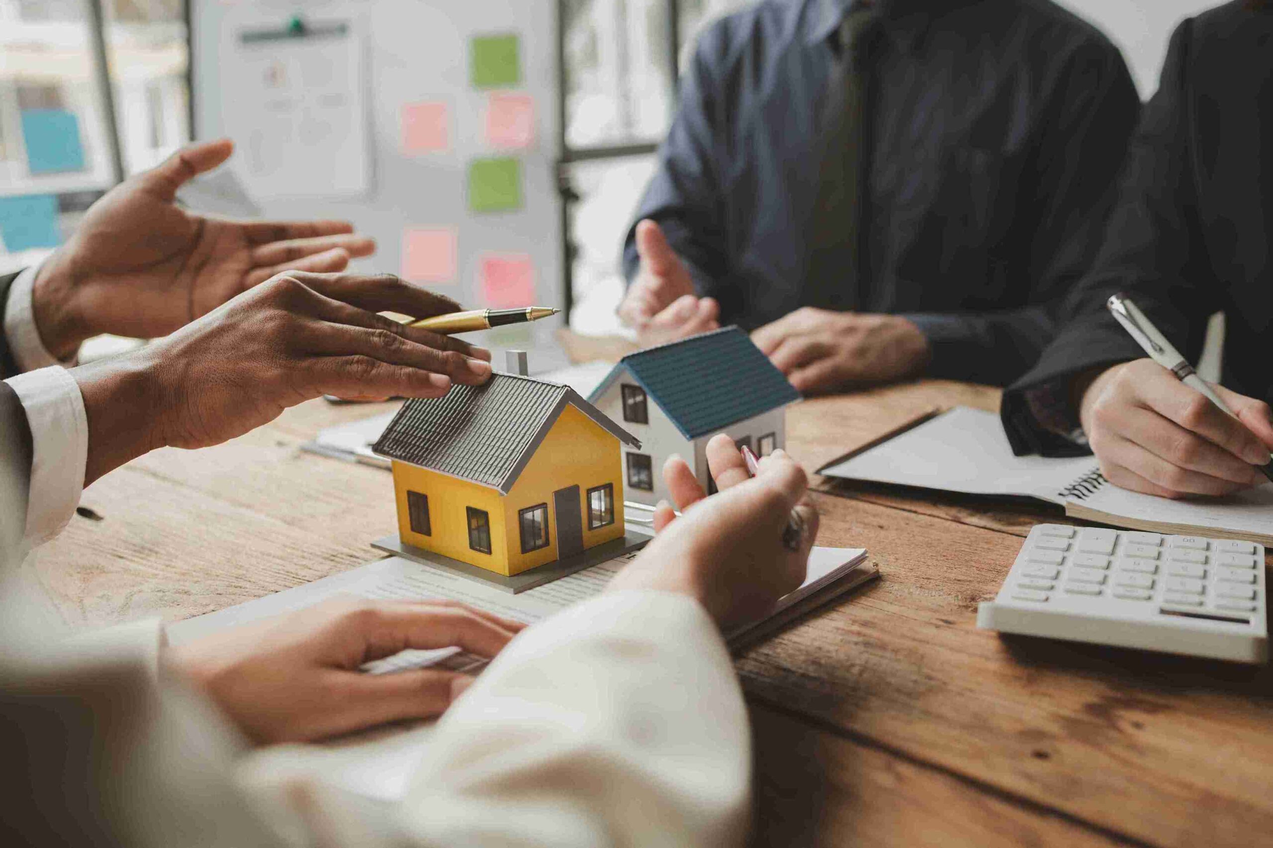 A diverse group of people discussing plans around a table featuring a detailed house model.
