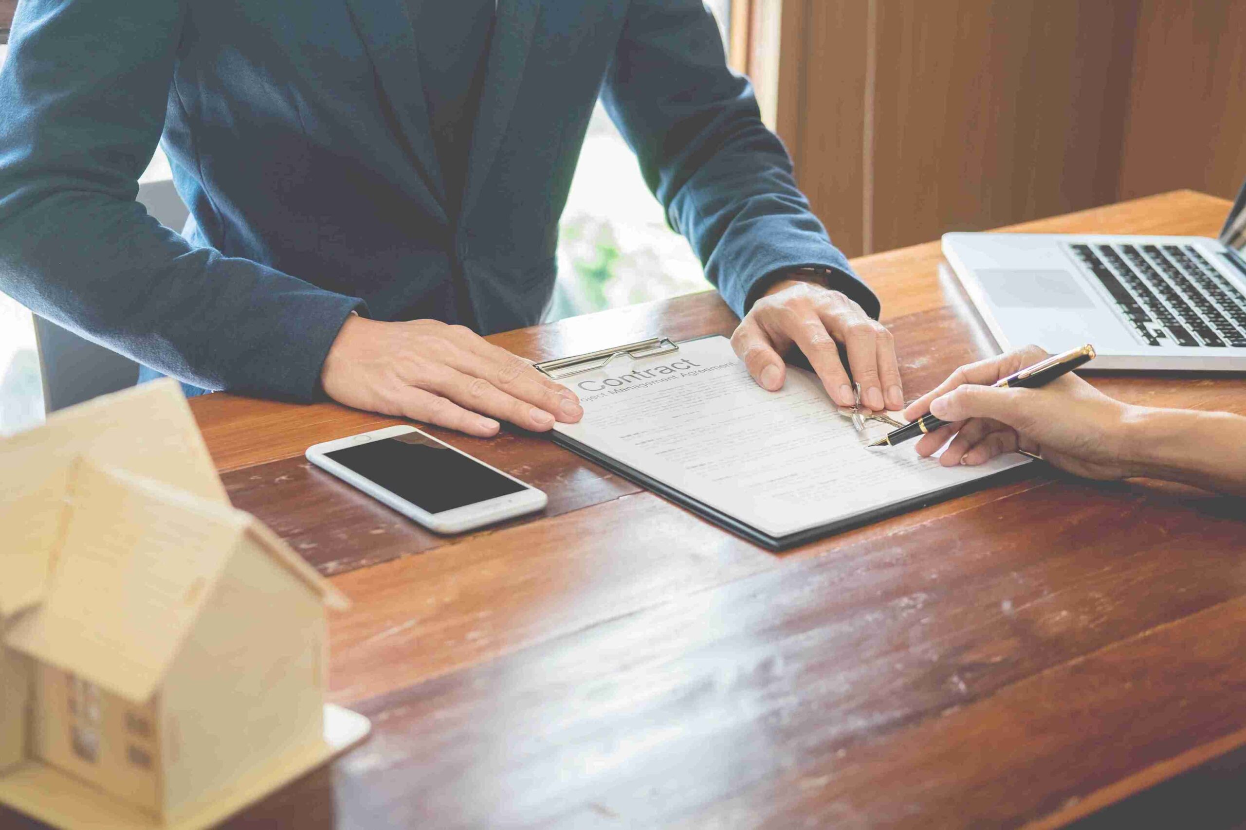 A real estate agent and a client are signing a contract at a table, smiling and discussing the agreement.