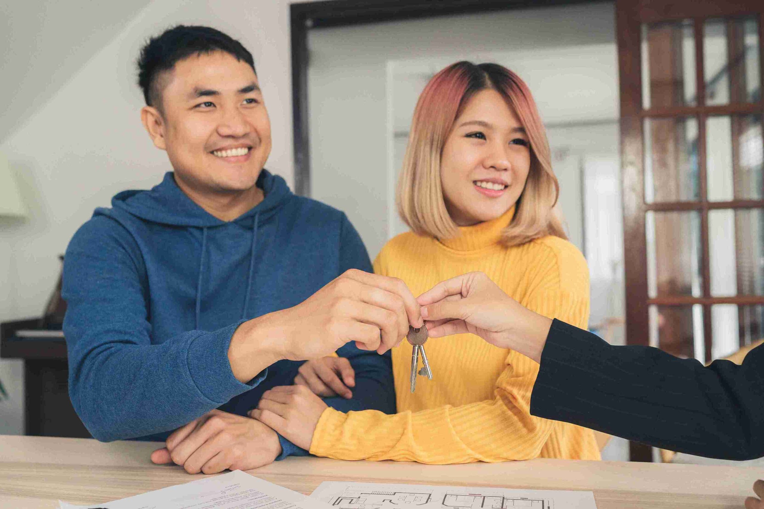 A happy couple holds keys to their new house, smiling and celebrating their milestone together.