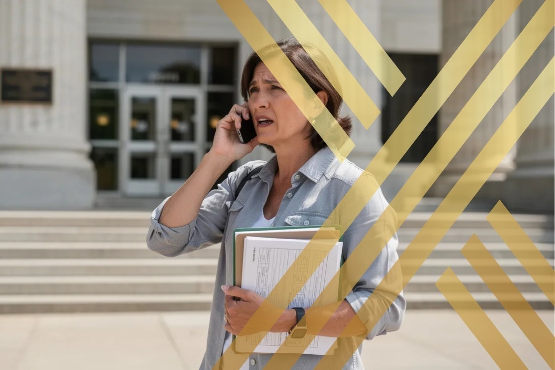 A family member stands outside a public building, holding important documents while discussing immigration rules or a deportation process affecting a foreign national on phone.
