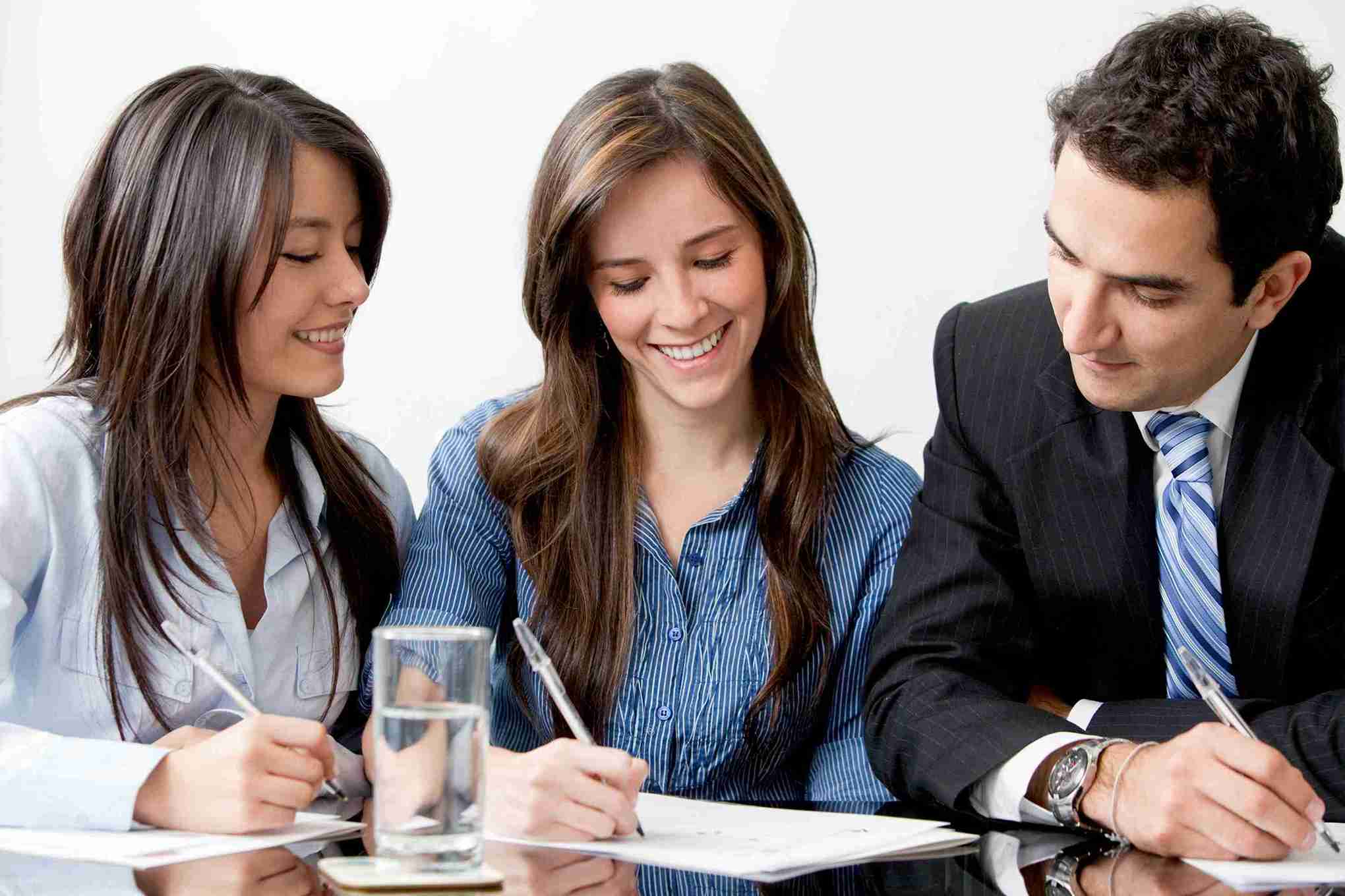 Three business professionals collaborate at a table, surrounded by papers and pens, engaged in discussion.