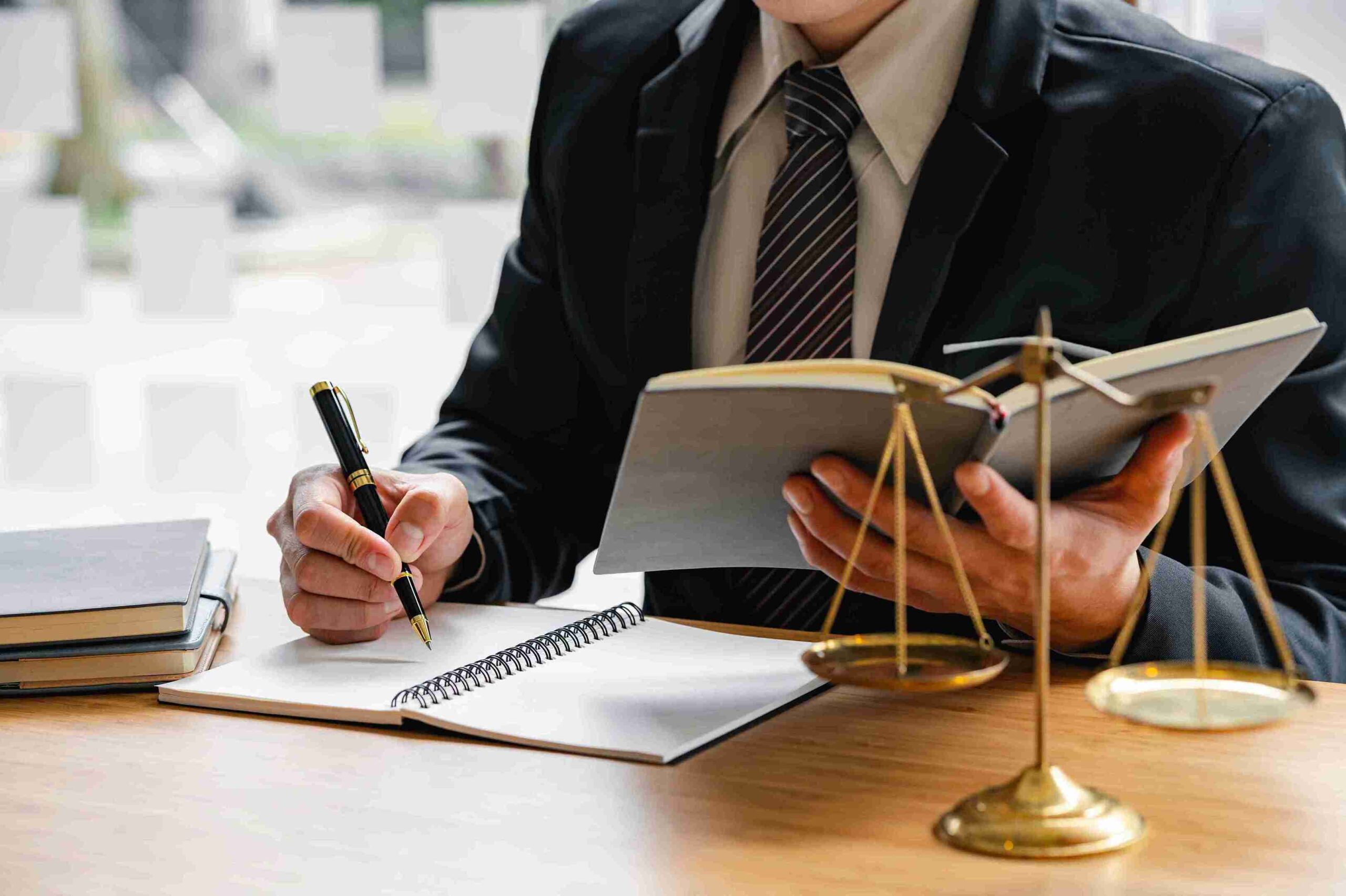 Lawyer focused on writing notes in a notebook, surrounded by legal documents and a pen on a desk.