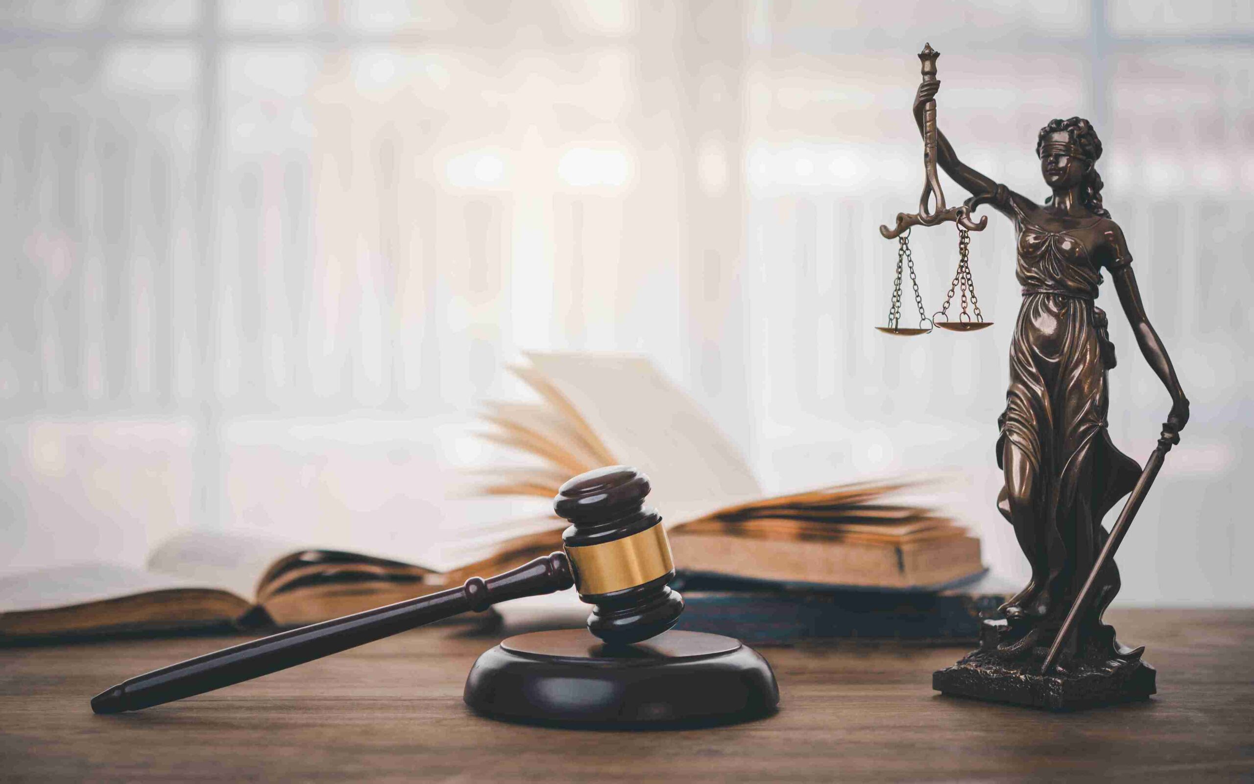 A statue of Lady Justice holding scales, alongside a gavel, on a polished wooden table.