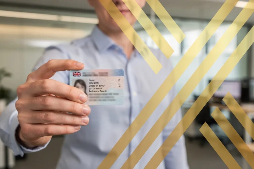 A person is standing in a UK office environment, holding a small credit-card-sized biometric residence permit (BRP) card, with their personal details blurred for privacy.