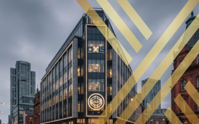 A sleek, modern corporate building at a busy intersection in Manchester at dusk, featuring the "AXIS Solicitors" logo prominently displayed on its facade and a glowing sign on the street level.